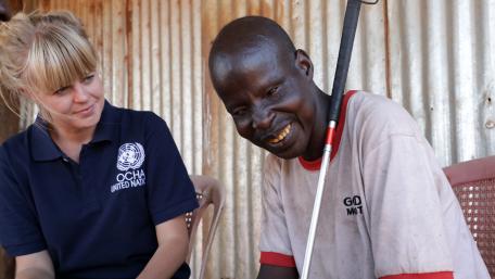 A blind men smiles next to a young humanitarian worker