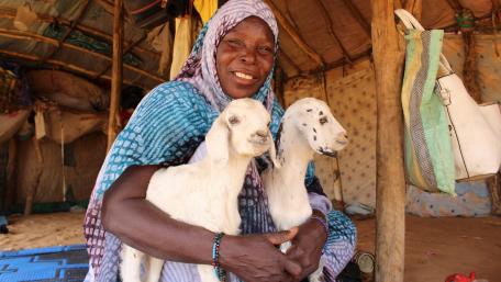 A woman smiles while holding ttwo sheep on her arms