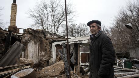 An old man in front of a destroyed house
