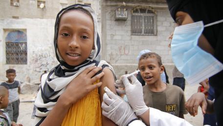 A girl is vaccinated in the street, while other children look