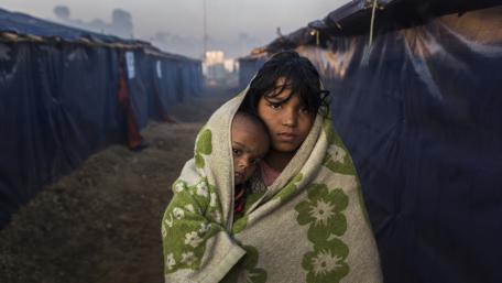 Two young girls in a refugee camp covered by a blanket