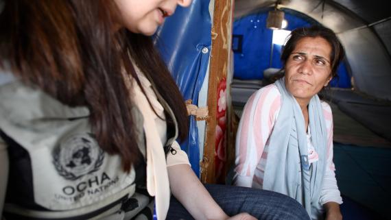A woman looks at a humanitarian worker who interviews her inside a tent