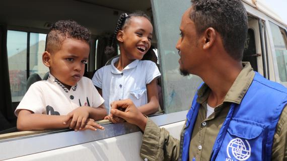 Two young children smile at a humanitaran worker from inside a van