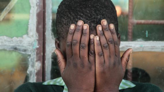A young boy covers his face with his hands