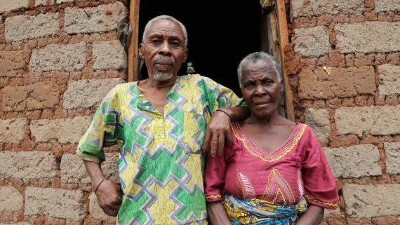 An older couple stand at the front of their home