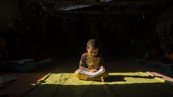 A Rohingya refugee child studies in his shelter