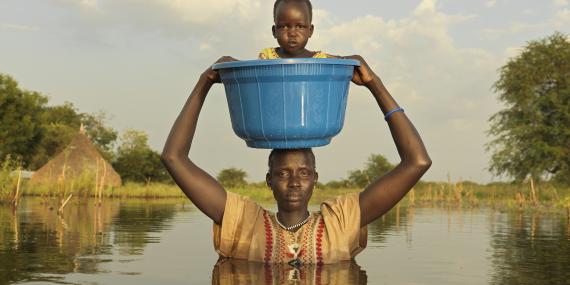 A mother carries her daughter  to dry land. “We make a sacrifice to bring our children to safety using a bucket”. 