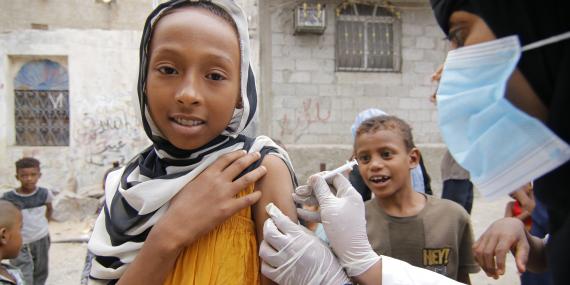 A girl is vaccinated in the street, while other children look